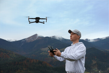 Young man operating modern drone with remote control in mountains