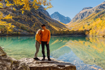 Travelling couple at crystal lake and autumnal mountains. Mountain lake and couple hikers