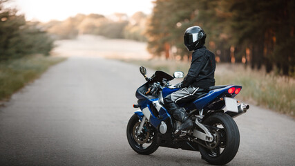 Fototapeta na wymiar Biker in a protective suit with a helmet. Motorcyclist in helmet and leather jacket on the road on a sports motorcycle