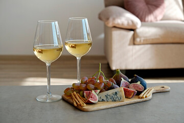 Two wineglasses of vintage chardonnay with delicious appetizers. Couple of glasses of white wine, italian breadsticks, figs and grapes. Interior background. Close up, copy space.