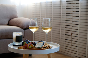 Two wineglasses of vintage chardonnay with delicious appetizers. Couple of glasses of white wine, italian breadsticks, figs and grapes. Interior background. Close up, copy space.