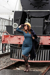 Young woman in retro styled clothes standing in front of vintage steam locomotive