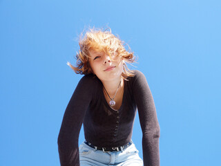 teenage girl with golden hair looking at the camera against the background of the sky, bottom view