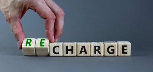 Charge or recharge symbol. Businessman turns wooden cubes and changes the word 'charge' to 'recharge'. Beautiful grey table, grey background. Business charge or recharge concept. Copy space.