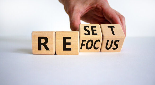 Refocus and reset symbol. Businessman turns cubes and changes the word 'refocus' to 'reset'. Beautiful white table, white background. Business refocus and reset concept. Copy space.