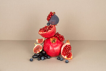 Fresh ripe pomegranate, fig slices, black grape, red currant, blueberry on beige background. Healthy balanced diet food. Delicious autumn fruits composition. Vitamins and antioxidants. Balance concept