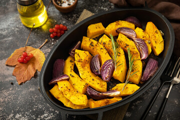 Pumpkins slice with rosemary and purple onion, baking fresh healthy food with spice on a dark stone...