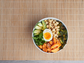 top view of an isolated Buddha Bowl on bamboo tablecloth with chickpeas, avocado, roasted broccoli...