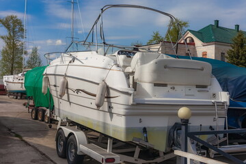 Rear view of the yacht on the beds with wheels on the shore against the background of a blue sky with clouds in summer