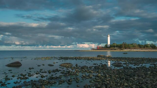 Time lapse of Swedish lighthouse Lange Erik on island in north of Oeland during sunset with dramatic moving clouds, stone coast in the front
