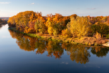 Autumn landscape. Bright colors of autumn by the river. Multicolored autumn trees in the sun on the river bank.
