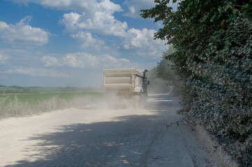 Industrial dump truck, transportation of stones, rides on a dusty road. Leaves. Career work