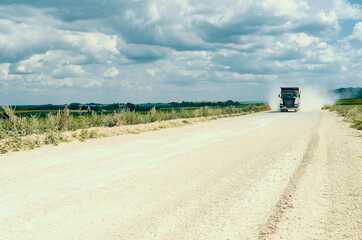 Industrial dump truck, transportation of stones, rides on a dusty road. Career work.Cloudy sky