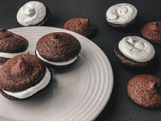 Chocolate sandwich cookies, baked biscuits stuffed with cream on a white plate on black background....