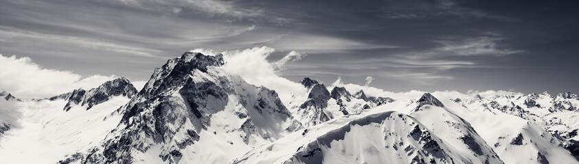 Fototapeta premium Black and white panorama of high snow-capped mountain peaks at windy winter day