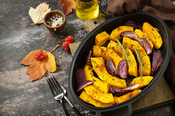 Baked pumpkins slice with rosemary and purple onion, baking fresh healthy food with spice on a dark stone background. Keto or paleo diet veggie vegan or vegetarian. 