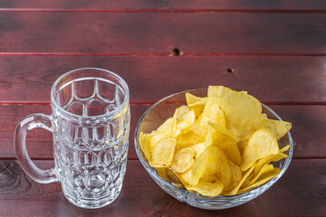 Сlose up view of empty beer mug and plate with chips isolation on wooden background.