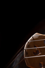 The bridge of an acoustic wood double bass with strings on a black background