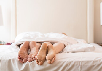 Couple in bed. View of bare feet of happy man and woman