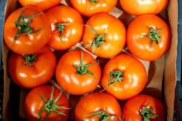 red tomatoes with green leaves in a box. they are on the shelf of the store. Close-up, top view, food wallpaper.