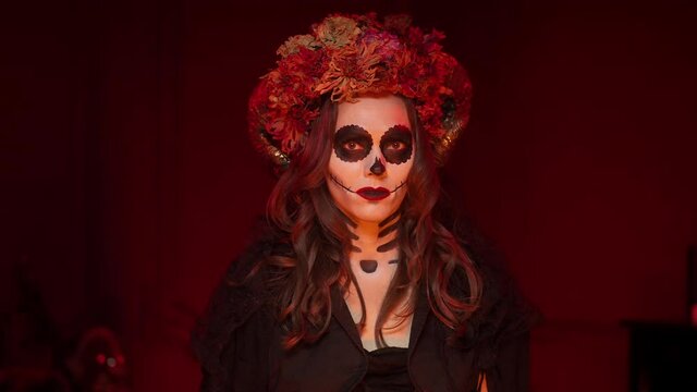 idea of witch image for Halloween in style of calavera skull with horns, dry flowers, painted eyes, sewn mouth in studio with light from fire. Woman makeup for day of dead