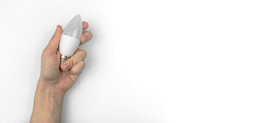 Hand with LED light bulb on a white table background with copy space, banner