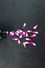 Pink pills with medicines are scattered from a black jar on a black background