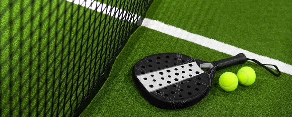 Closeup view of a paddle racket and balls in a padel tennis court near the net. Green background with white lines. Sport, health, youth and leisure concept. Sporty equipment. White lines in background