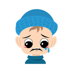 Boy with crying and tears emotion, sad face, depressive eyes in blue knitted hat. Cute kid with melancholy expression in autumnal or winter headdress. Head of adorable toddler