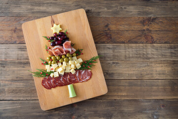 Christmas tree shaped cheese and charcuterie board with wooden background. Top view. Copy space.