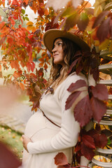 Fototapeta na wymiar Pregnant girl in a hat and a white dress in autumn at sunset in the park