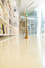 A raw brass rotary trumpet standing on its bell on a reflective light colored floor in the library...