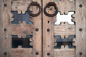 An old wrought iron door knocker on an old carved wooden door in the Russian style.  The forged handle of the handmade hammer is made of iron close-up against the background of a wooden door. 