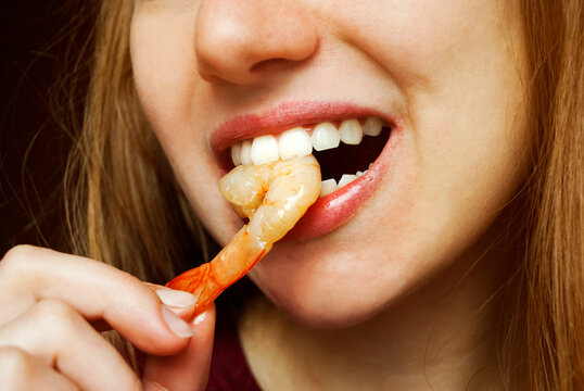 A woman with her hands eats a large appetizing shrimp. Selective focus. Mouth bites shrimp, close-up. 