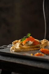 Crepes (big thin pancakes) with red caviar, and cream cheese or sour cream with basil leaf on dark background. Beautiful light, selective focus, copy space. Tasty breakfast, dark mood photo concept.