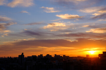 都市の夜明け、早朝ビルの隙間から太陽が昇り辺りはオレンジ色に染まる。ビルはシルエットに浮かぶ