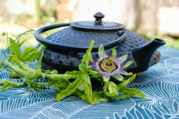 Obraz na płótnie Canvas Cast iron tea kettle and passionflower on a turquoise tablecloth in the garden. Sunlight.