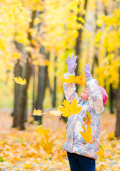 A 5-year-old girl in the autumn in a city park, having fun and throwing up yellow leaves fallen from the trees