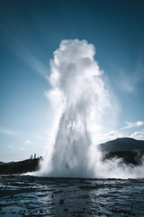 Geysir in Island vor der Sonne mit blauem Himmel