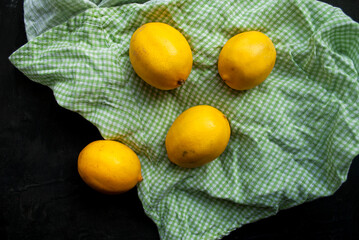 Four lemons are on a kitchen towel. Black background, top view. 