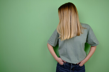 Girl model posing near a green wall in a green t-shirt and jeans. Hand gestures and emotions. Studio shot of a girl. Emotion and beauty concept. Casual wear