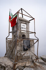 Musala summit stone on Rila mountain and Bulgarian flag on a misty, foggy day with an icon of St John of Rila