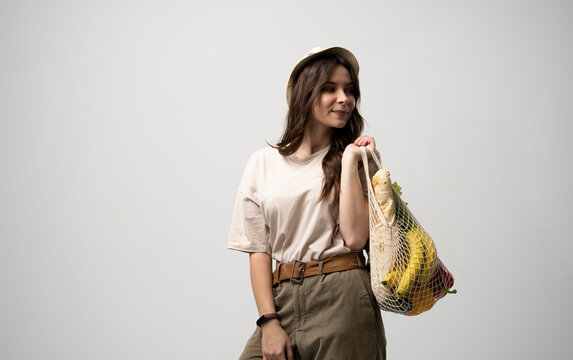 Zero waste concept. Young brunet woman holding reusable cotton shopping mesh bag with groceries from a market. Concept of no plastic. Zero waste, plastic free. Sustainable lifestyle.