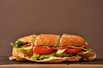 baguette stuffed with salami, tomato, cheese and lettuce on the cutting board