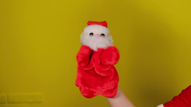 Soft puppet toy of santa claus on hand. Santa claus puppet on yellow background. Close up. Concept of puppet show and new year holidays.