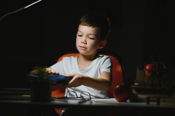 Boy learn lessons in the home setting at the table in the light of a table lamp.