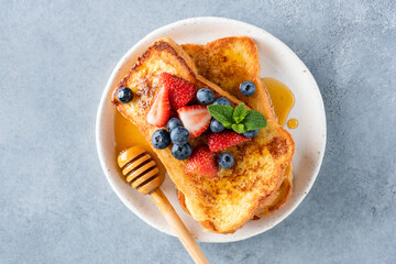 French toasts with honey and fresh berries on white plate, table top view. Sweet breakfast or...