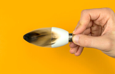 Hand with broken after fire LED light bulb. Concept of electrical short circuit. Burning wire in house, dangerous, failure. Home safety. Top view, orange background photo