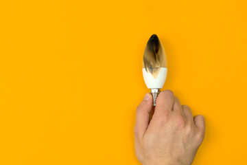 Hand with burned LED light bulb. Concept of electrical short circuit. Burning wire in house,...