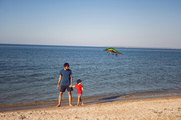 father and son are standing on a sandy beach by the sea and launch toy striped kite in the summer on vacation